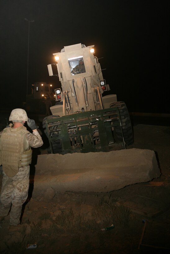 Cpl. Michael Robinson, a 22-year-old motor transport operator from Glenmore, Pa., with 2nd Combat Engineer Battalion, attached to 1st Battalion, 9th Marine Regiment, Regimental Combat Team 1, directs a heavy equipment operator towards a concrete barrier in Ramadi, June 18. Marines with 2nd CEB are doing their part to help clean up the streets and return a sense of normalcy to the people of Ramadi by removing any unnecessary materials resembling signs of war throughout the city.