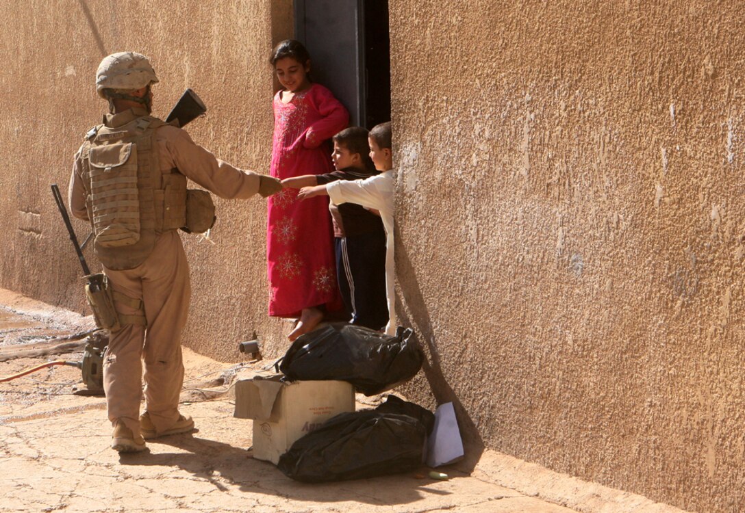Handing candy out to Iraqi children, Cpl. Steven M. Barrientos, a radio operator with Mike Battery, 3rd Battalion, 14th Marine Regiment, 2nd Light Armored Reconnaissance Battalion, Regimental Combat Team 5, assists the Iraqi Police with a patrol in Rutbah, Iraq, June 18.  Marines with Mike Battery have been working with the IP to make them more efficient at patrolling.