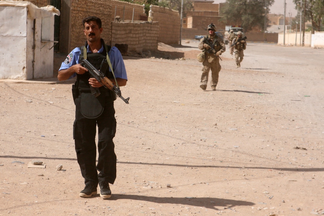 Chief Warrant Officer Mohammed Ahmid Kolef, a patrol master with the Rutbah Iraqi Police, is assisted by Marines with Mike Battery, 3rd Battalion, 14th Marine Regiment, 2nd Light Armored Reconnaissance Battalion Regimental Combat Team 5, in patrolling techniques during a joint patrol through Rutbah, Iraq, June 18. During the patrol, the group walked through the city streets engaging with citizens.