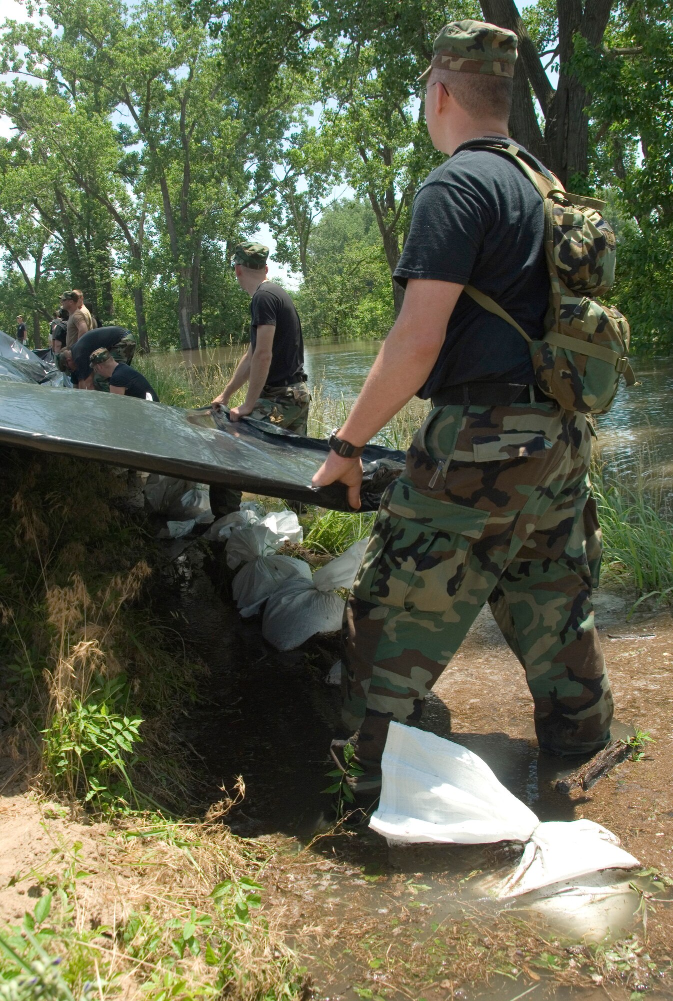 Airmen from the Illinois Air National Guard wade in knee-deep water to spread sheets of plastic over reinforced levees along the Mississippi River June 19 near Pleasant Hill, Ill. The plastic sheets prevent erosion that could cause the levee to fail and flood thousands of acres of farmland and homes. (U.S. Air Force photo/Master Sgt. Jack Braden) 