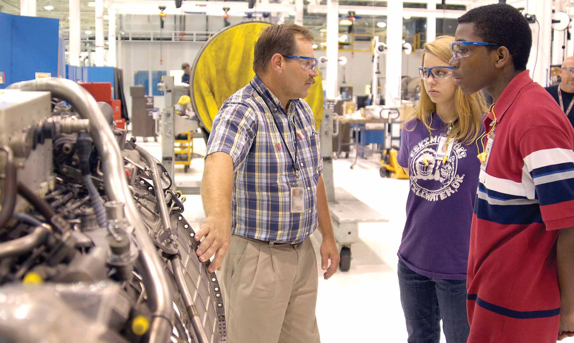 Facillities engineer David Delsigne shows high school juniors Michelle Danser and Patrick Saah  a GE 110-100 lower duct as he leads them through Bldg. 3001 shops during a recent Job Shadowing visit.  The Tinker program offers students opportunities to see real-world work environments of professionals like Mr. Delsigne, a 76th Propulsion Maintenance Group engineer.  (Air Force photo by Margo Wright)
