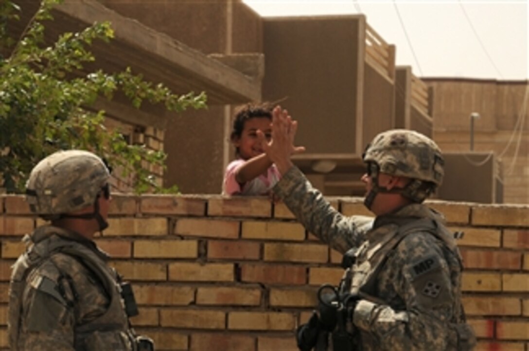 U.S. Army Sgt. Matt Radcliffe, a military policeman from the 3rd Brigade Combat Team, 4th Infantry Division, gives a high five to a young Iraqi girl while Spc. Martin watches during a patrol through the Thawra 1 neighborhood of Sadr City, Iraq, on June 16, 2008.  