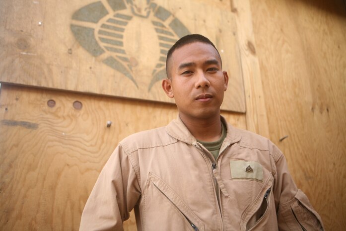 Standing in front of his unit symbol, Cpl. Seth Chimm, Biometrics Automated Toolset supervisor of Mike Battery, 3rd Battalion, 14th Marine Regiment, Regimental Combat Team 5, displays how proud he is to be a Marine in Rutbah, Iraq, June 23. Born in a refugee camp in the Philippines, Chimm, 24, from Chattanooga, Tenn., joined the Marines to repay a debt he feels he owes to the United States.::r::::n::