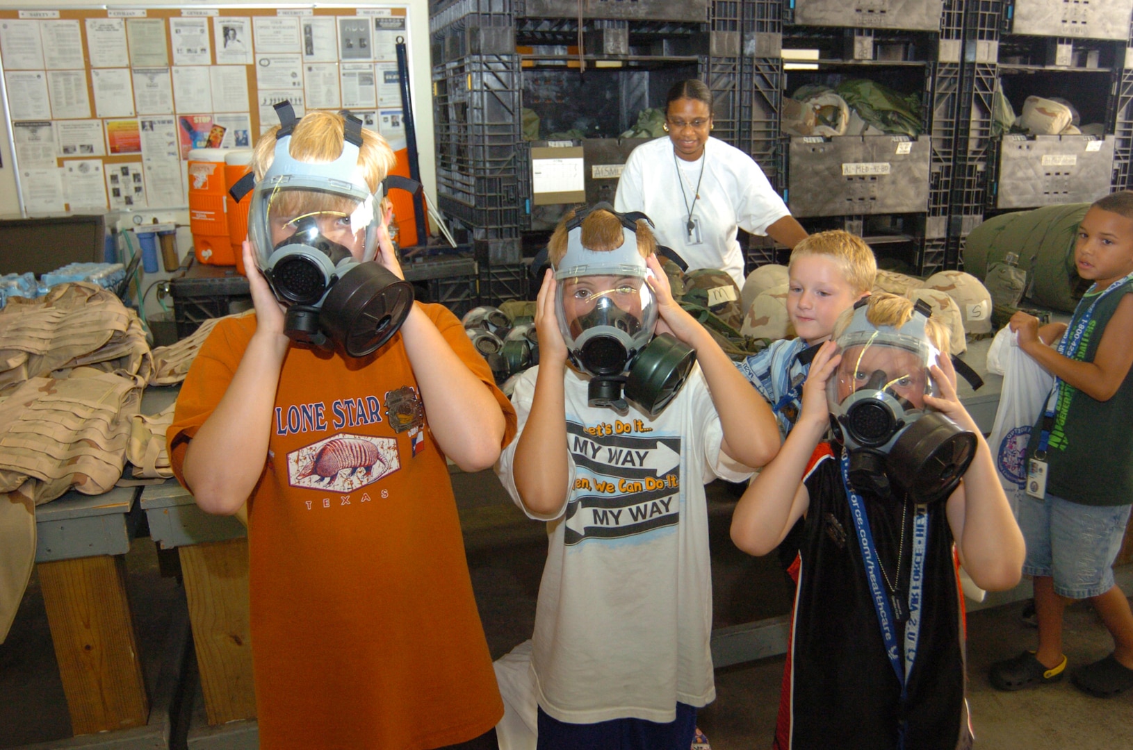 Joseph Leachman, 9, Caden Tucker, 8, and Andre Houk, 6, demonstrate the proper fit and wear of the MCU-2 series gas mask during their group?s rotation through the warrior deployment facility here June 13. The trio were three of more than 100 youth center and military family participants in this year?s Operation Families Learning About Global Support sponsored by the Airman and Family Readiness Center. (U.S. Air Force photo by David Terry)