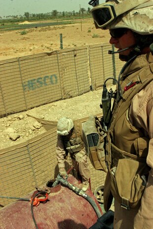 Lance Cpl. Justin W. Roberts, a 21-year-old 240-Golf gunner from Glenrose, Texas, provides security for Lance Cpl. David A. Brown, a 20-year-old Motor-T operator from Duncanville, Texas, while he re-fuels a fuel tank at Joint Security Station (JSS) Mobile during a re-supply mission June 22. The Marines from Combat Trainâ??s 1 and 2 of 2nd Battalion, 24th Marines, make sometimes daily trips to deliver essential tools and supplies to the infantry companies whenever they need.