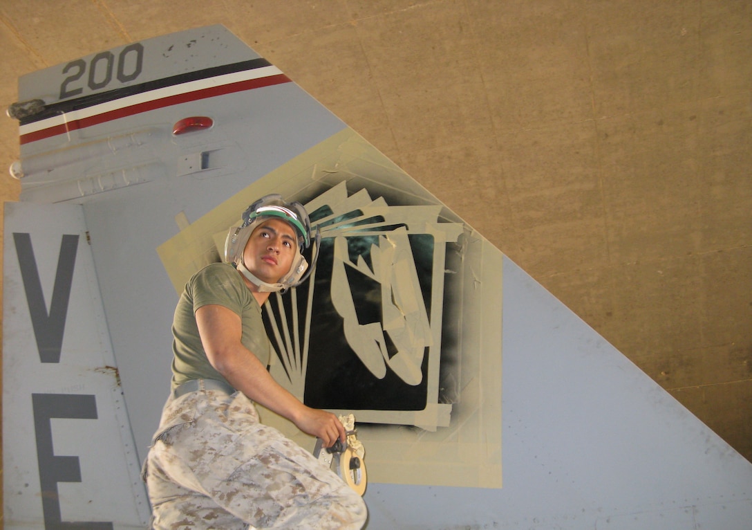 Sergeant Miguel Agudo, a corrosion control technician with Marine Fighter Attack Squadron 115, 3rd Marine Aircraft Wing (Forward), checks a visual aide while stenciling the squadron’s former emblem onto the tail of an F/A-18 Hornet. The aircraft will fly the “Joe’s Jokers” logo from July 1 until the end of the squadron’s current deployment in honor of Maj. Joe Foss, former commanding officer of VMFA-115 during World War II.