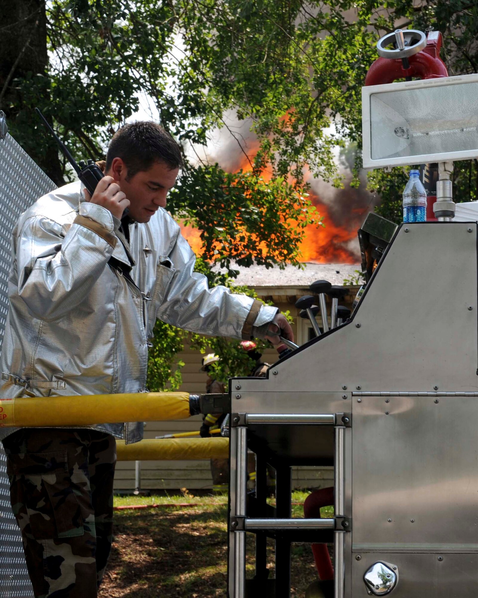 SHAW AIR FORCE BASE, S.C.-- Senior Airman Nicholas Mintz, 20th Civil Engineering Squadron firefighter, works the water pump with direction from other firefighters on the radio as a house fire rages on behind him June 20. The house is in an area marked for demolition and was not occupied. (U.S. Air Force Photo/Staff Sgt. Henry Hoegen)