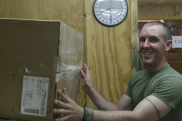 Cpl. John Chastain, a rifleman with the jump platoon, Task Force 2nd Battalion, 2nd Marine Regiment, Regimental Combat Team 5, sorts through packages sent by the recently started Parent Network of the battalion at Camp Al Qa'im, Iraq, June 23. The network has sent numerous packages containing personal care items and other gifts. The network was started so that parents could obtain information or ask questions about their Marines serving in Iraq.