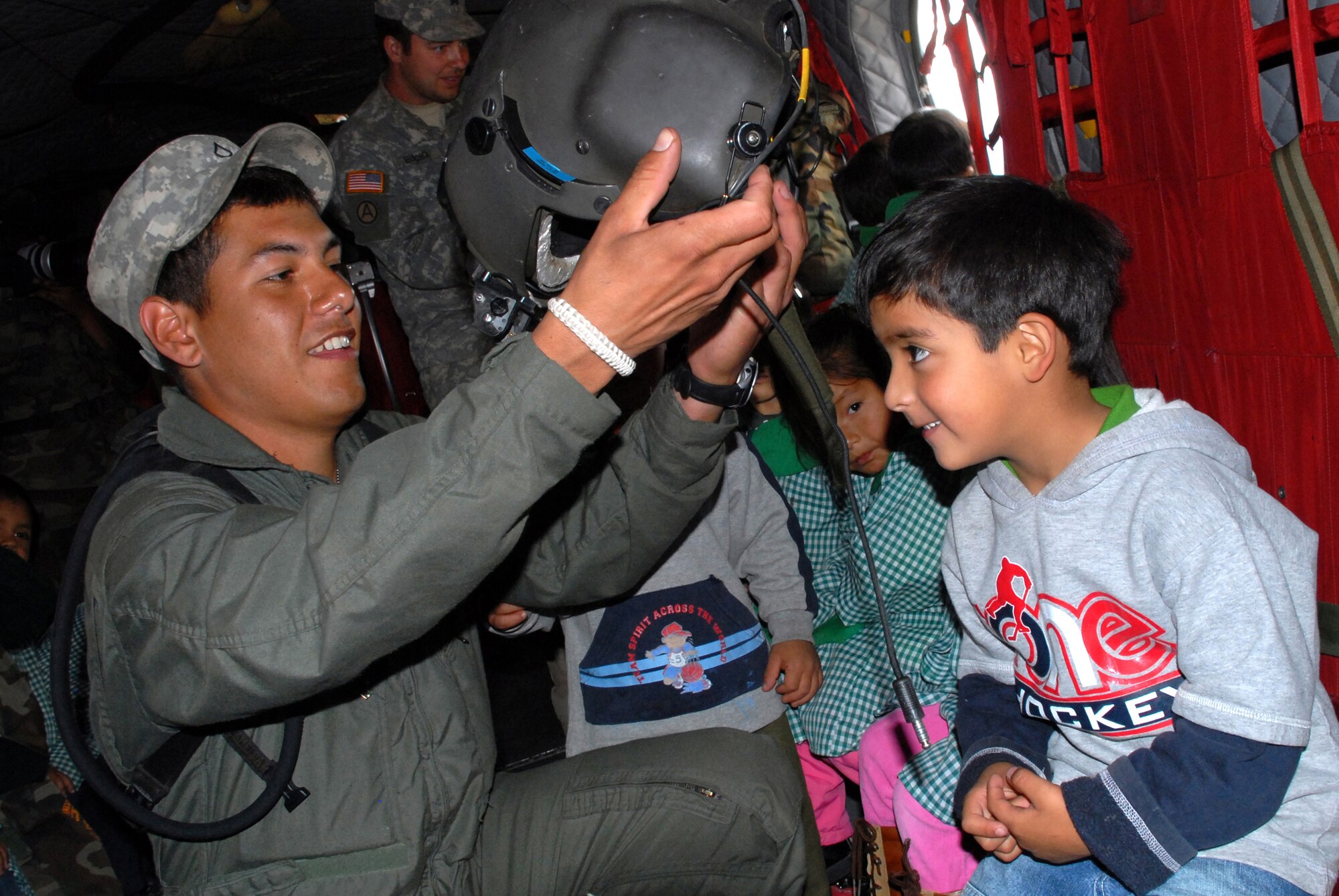 U.S. Army Specialist Josue Moises Coranado-Iglesias, a helicopter engineer assigned to Task Force New Horizons, places a flight helmet on the head of Jose Stephano Diez Zamora, 4, June 11, during their tour of a U.S. CH-47 Chinook helicopter currently assigned to Task Force New Horizons and residing in Los Cabitos, Peru. (U.S. Air Force photo/Tech. Sgt. Kerry Jackson)