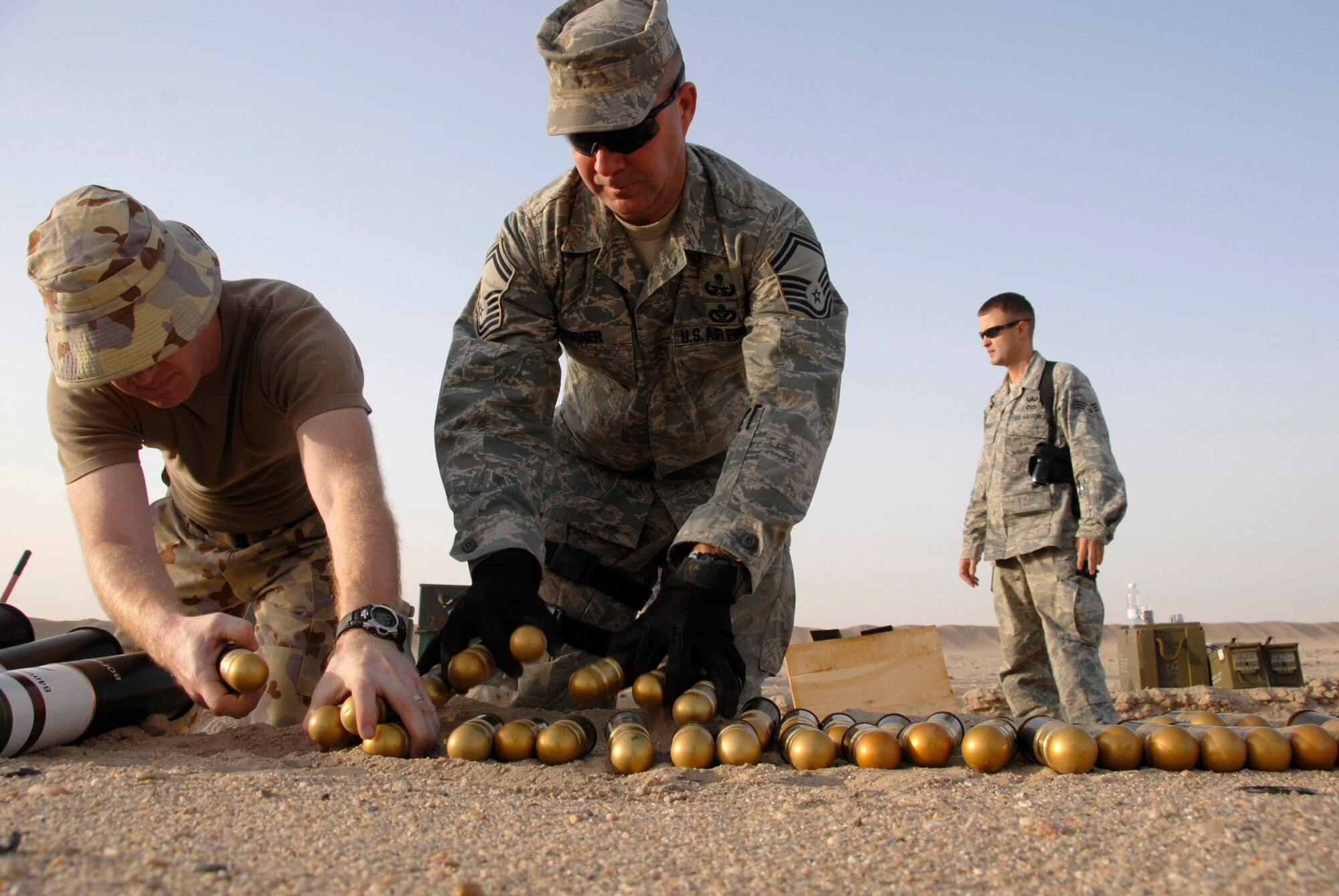 Australian army ammunition technician Warrant Officer Class Two Neil Snape (from left to right), Senior Master Sgt. Russell Corner and Senior Airman Charles Howell help move 40 millimeter high explosive dual purpose rifle grenades for disposal in preparation for a controlled detonation June 20 at an explosive ordnance disposal range in Southwest Asia. The joint detonation also provided an opportunity for the U.S. and coalition forces to enhance their relations while learning some of the slight differences in operating procedures. Sergeant Corner and Airman Howell are from the 386th Expeditionary Civil Engineer Squadron Explosive Ordnance Disposal Flight. (U.S. Air Force photo/Staff Sgt. Patrick Dixon) 
