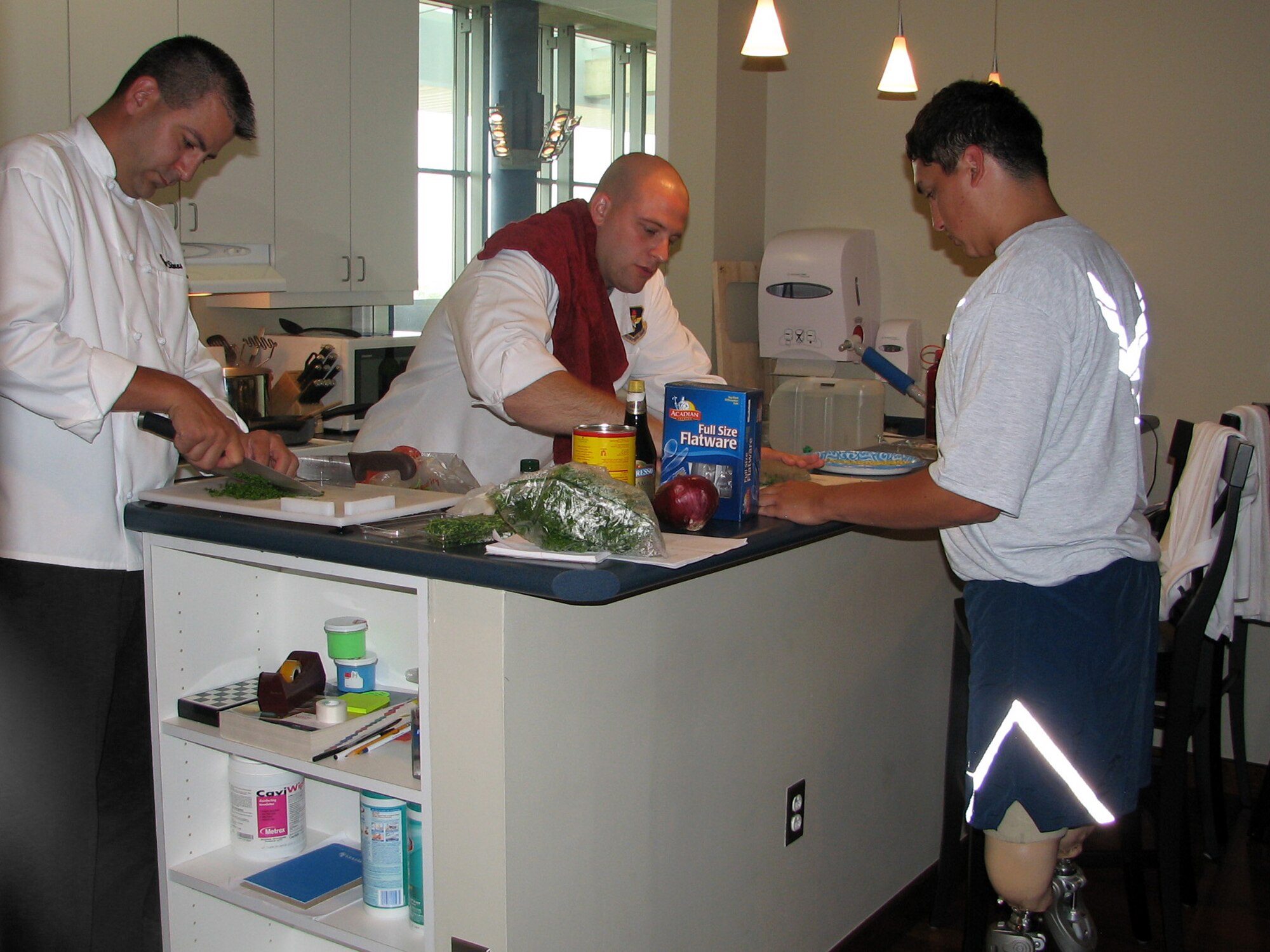 Tech. Sgt. Jason Simas and Staff Sgt. Michael Leo. Prepare a lavish fest for Airmen at the Center for the Intrepid. Airman 1st Class Kevin Krogh assists in the preperation. The Sergeants are enlisted aides to the AETC commander and vice commander. They volunteered their culinary talents to support sevice members in treatment at the center. (U.S. Air Force photo/Beverly Simas)