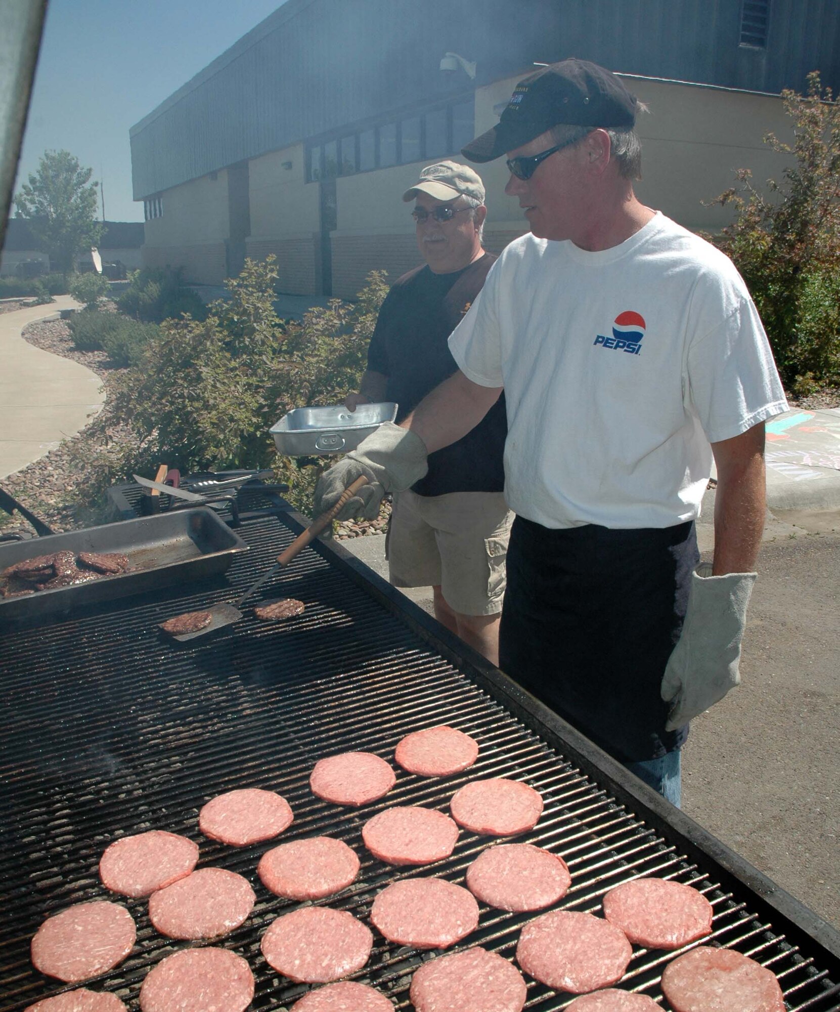 Dan Binstock, owner of Fuddruckers, flips burgers on the grill as Ray Hoffman prepares to place cooked burgers in a pan during the Youth Program Center’s annual Chalk It Up! competition Wednesday. (U.S. Air Force photo /Airman 1st Class Dillon White)