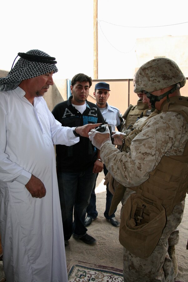 Lance Cpl. Nelson Flores of Headquarters and Service Company, 2nd Battalion, 25th Marine Regiment uses the Handheld Interagency Identification Detection Equipment to record biometrics information on the inhabitant of a house where his squad found explosive-making materials during a predeployment training exercise here June 26, 2010.  Nelson is assisted by an Iraqi interpreter and Iraqi police officer (rear), both role players in the scenario.