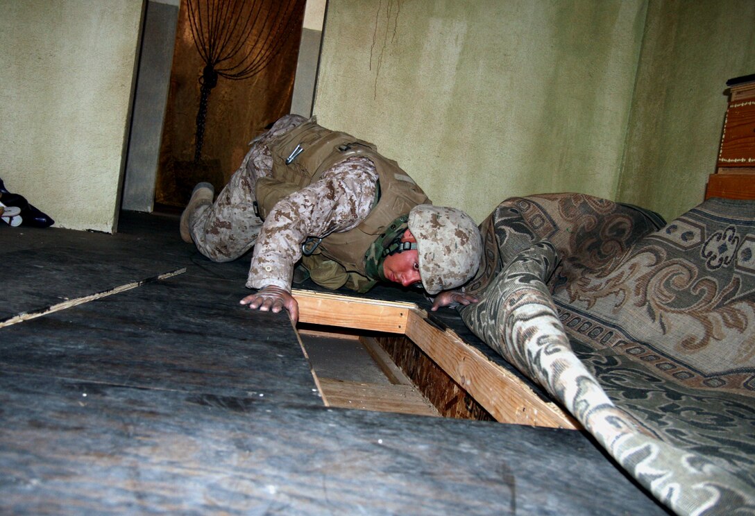 Lance Cpl. Brandon Ehret, a Company E, 2/25 rifleman, uncovers a hidden trap door leading to a weapons cache under the floor of a bedroom during an occupied building search as part of the Search and Tactical Site Exploitation course here June 26, 2008.  Training was facilitated by the U.S. Joint Improvised Explosive Device Defeat Organization.