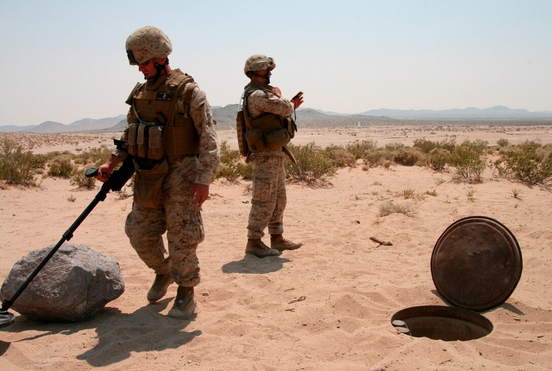 After uncovering a buried weapons cache in the desert, Lance Cpl. Alexander Vassilopoulos uses an F-3 metal detector to look for other caches in the area during a training exercise here June 26, 2008.  Cpl. Joseph Shutta calls in the report.   Under the mentorship of course instructors, reserve Marines from 2nd Battalion, 25th Marine Regiment learned to identify common markings used by insurgents to hide weapons, explosives and other items underground.  Both Vassilopoulos and Shutta are assaultmen with Weapons Company, 2/25.