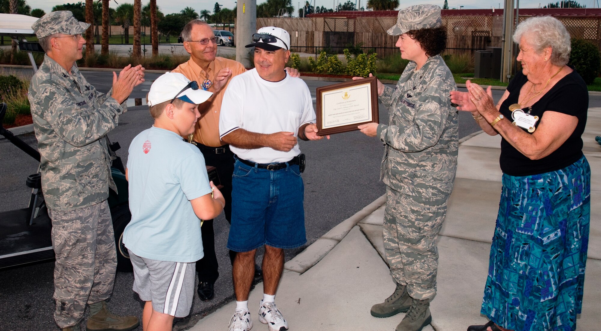 Project Emeritus volunteer Lou Dalmau (center in white shirt) receives a plaque from 45th Space Wing Commander Susan Helms Tuesday morning at the Manatee Cove Golf Course. A retired Air Force technical sergeant, Mr. Dalmau has accumulated more than 3,000 volunteer hours ferrying customers around the course in the shuttle golf cart he operates. (U.S. Air Force photo by Jim Laviska).