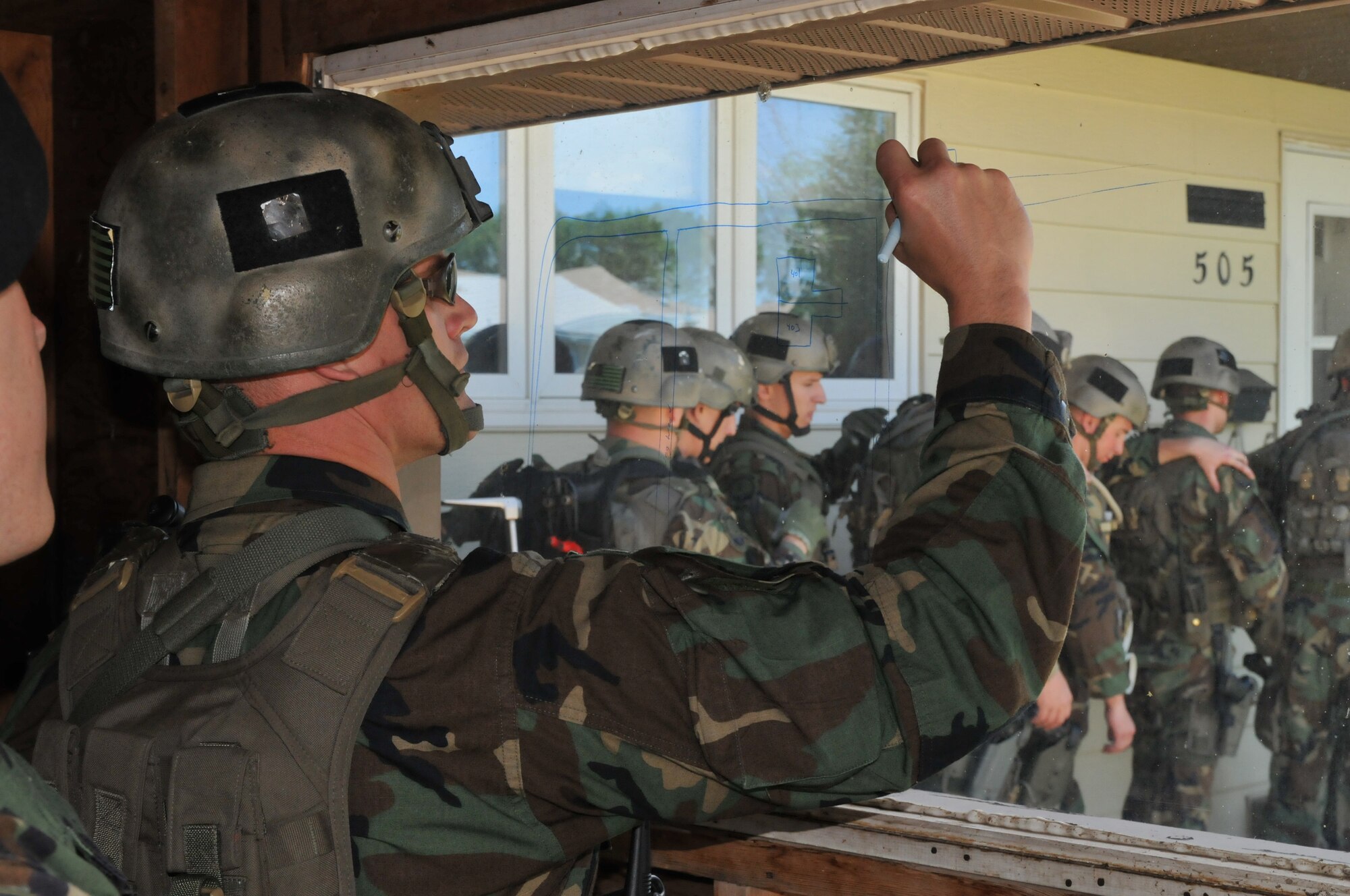 Tech. Sgt. Heath Adams, 341st Security Forces Group tactical response force, draws a plan of attack, while assault team prepares for assault during an exercise June 23. The exercise consisted of responding to a hostage situation in the housing area on base. (U.S. Air Force photo/John Turner)