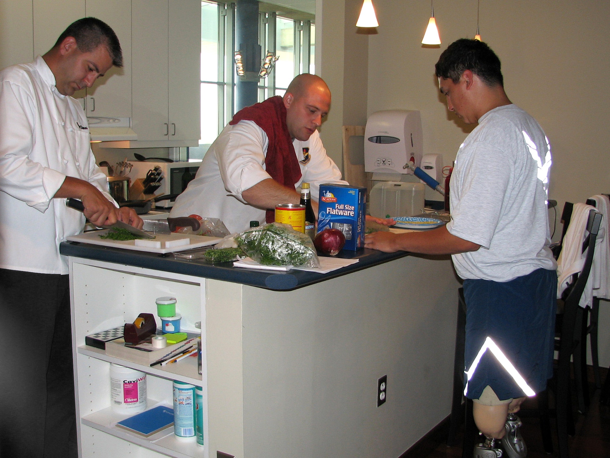 Tech. Sgt. Jason Simas and Staff Sgt. Michael Leo prepare a meal for Airmen at the Center for the Intrepid June 24 in San Antonio. Airman 1st Class Kevin Krogh assists in the preperation. The sergeants are enlisted aides to the Air Education and Training Command commander and vice commander. They volunteered their culinary talents to support sevicemembers in treatment at the center. (U.S. Air Force photo/Beverly Simas) 
