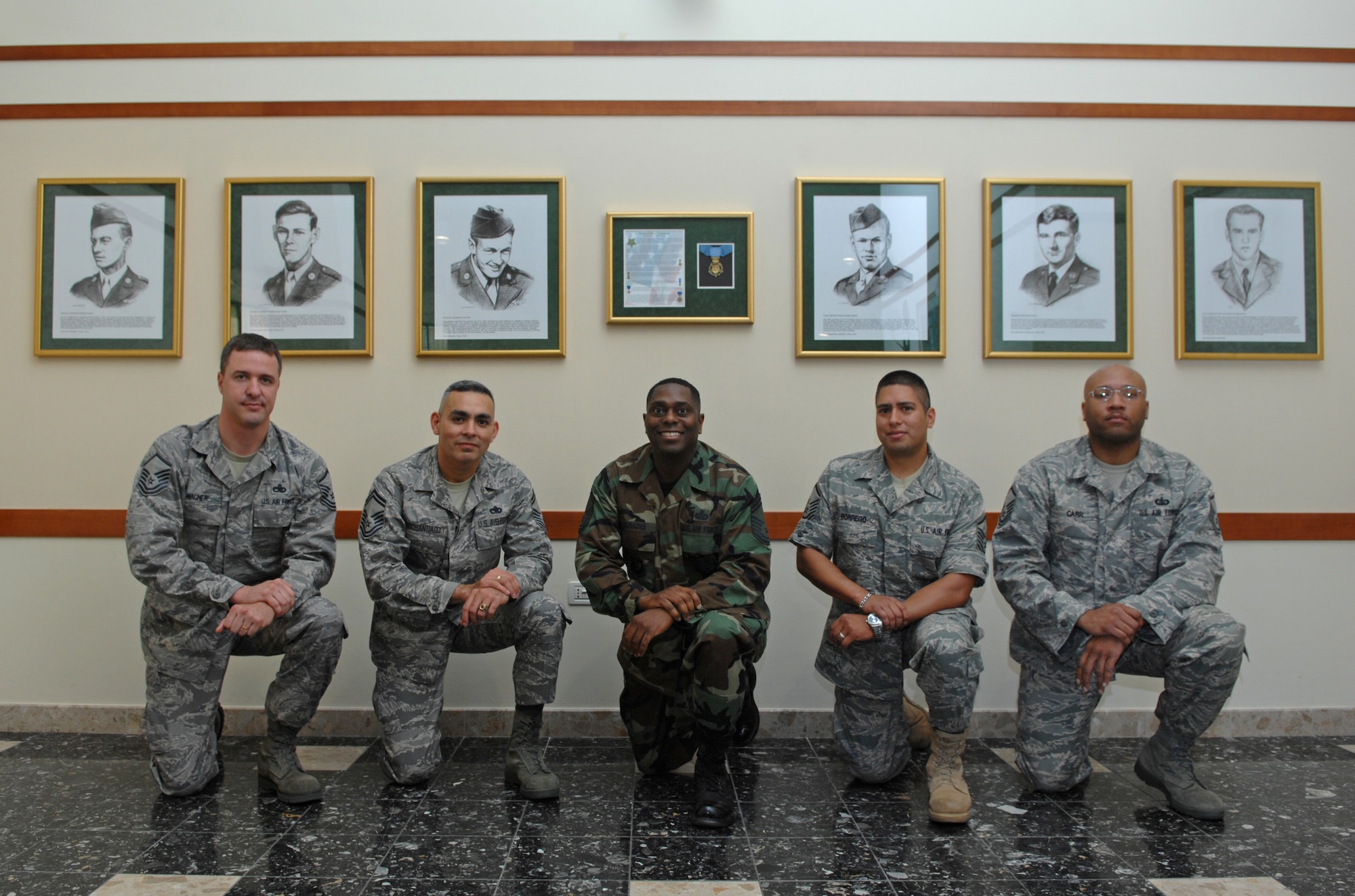 Members of the Aviano Enlisted Project Team kneel in front of a Medal of Honor recipients display. Located in the La Dolce Vita, six heroic Airmen are recognized for choices only Airmen truly committed to the Air Force Core Values would make, with some making the ultimate sacrifice.