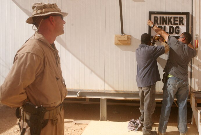 Gunnery Sgt. Curtis T. Rinker, company gunnery sergeant, Headquarters and Service Company, 2nd Light Armored Reconnaissance Battalion, Regimental Combat Team 5, watches as the sign of the new internet and phone center is mounted after the center was named after him at Camp Korean Village, Iraq, May 28. The building for the new internet and phone center was named after Rinker because of his hard work building it.  The new center, which took about a month to complete, has more than 16 computers and 10 phones for service members to use.::r::::n::
