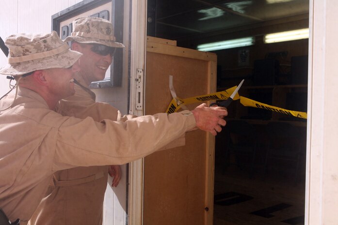 Cutting the ribbon of the new internet and phone center, Lt. Col. Russell E. Smith (Inside), 43, commanding officer, 2nd Light Armored Reconnaissance Battalion, Regimental Combat Team 5, and Gunnery Sgt. Curtis T. Rinker, company gunnery sergeant, Headquarters and Service Company, 2nd LAR, open the new center for business at Camp Korean Village, Iraq, June 28. The center was named after Rinker because of his hard work building the additional source of communication between service members and their families.::r::::n::