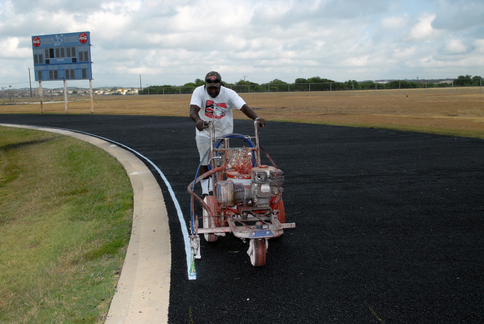 Rudy Roland, a 14-year employee with the Vibra-Whirl company, which is based in Panhandle, Texas, uses a machine to paint stripes on the new track surface at Randolph High School stadium. (U.S. Air Force photo by Rich McFadden)