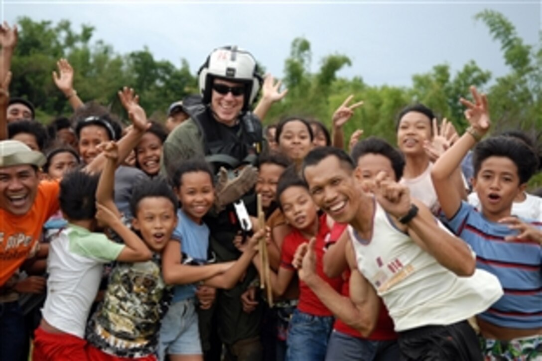 U.S. Air Force Airman John Baker poses for a photo with smiling residents of  Panay Island, Republic of the Phillipines, after he and other "Black Knights" of Helicopter Anti-Submarine Squadron delivered typhoon relief supplies, June 28, 2008. The aircraft carrier USS Ronald Reagan is off the coast of Panay Island providing humanitarian assistance and disaster response in the in the wake of Typhoon Fengshen.