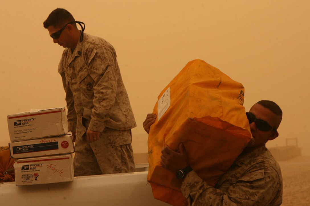 Staff Sgt. Jaime Benavides, linguist manager, and Cpl. James Whitehead, administrative clerk, both with Headquarters Company, Regimental Combat Team 5, unload care packages during a dust storm on Camp Ripper, Iraq, June 30.  The care packages where sent by Words of Comfort, Hope and Promise, a military outreach group in San Clemente, Calif.  Since arriving in Iraq in January, RCT-5 has received hundreds of care packages from groups and communities in Southern California.::r::::n::