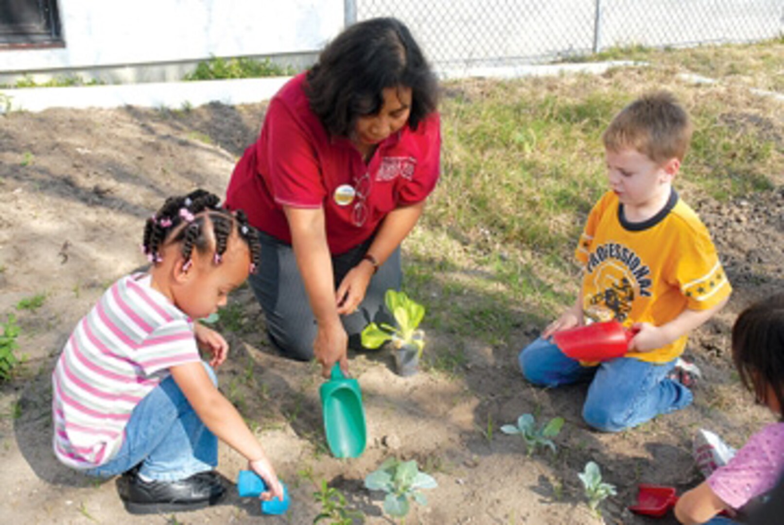 Ana Guadron, a caregiver at the Randolph Child Development Center, shows Alyssa Forehand, 3, and Hayden Holcombe, 5, how to use a shovel in the center’s garden.