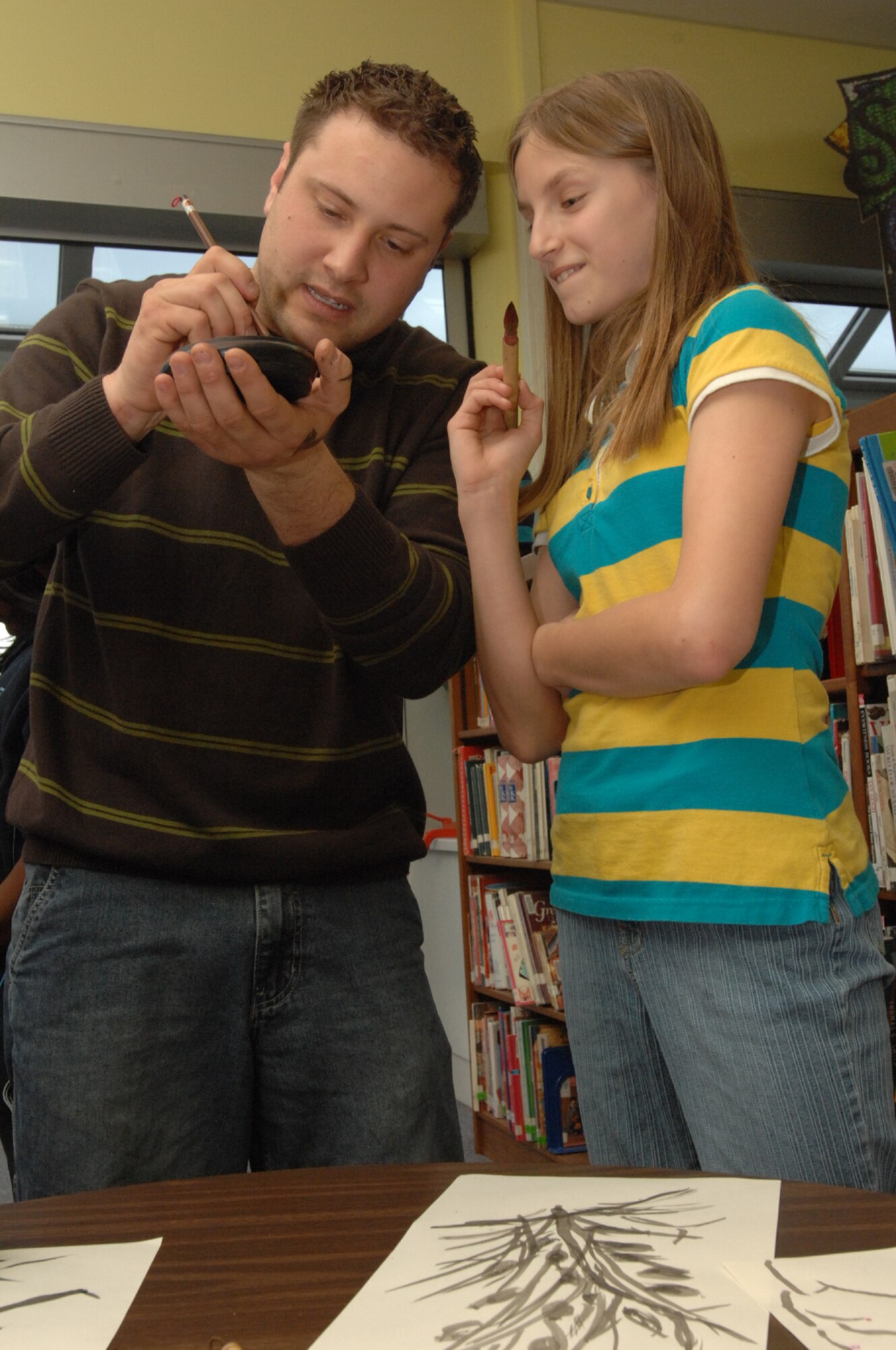SPANGDAHLEM AIR BASE, Germany -- Mikayla Dumuers, daughter of Danniel Demuers, looks on as Senior Airman Vito Cipolla, 52nd Medical Group pharmacy, demonstrates how to apply red ink to a calligraphy brush. Spangdahlem Middle School students spent the day learning about Ancient China and East Asia Feb. 27, 2008. (U.S. Air Force photo/Airman 1st Class Jenifer Calhoun)