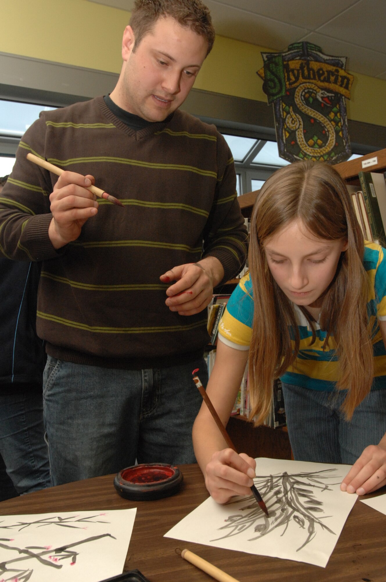 SPANGDAHLEM AIR BASE, Germany -- Senior Airman Vito Cipolla, 52nd Medical Group pharmacy, watches as Mikayla Dumuers, daughter of Danniel Demuers, paints red flowers on her East Asian brush painting of bamboo and leaves at Spangdahlem Middle School Feb. 27, 2008. East Asian brush painting is a detailed art also known as calligraphy. (U.S. Air Force photo/Airman 1st Class Jenifer Calhoun)
