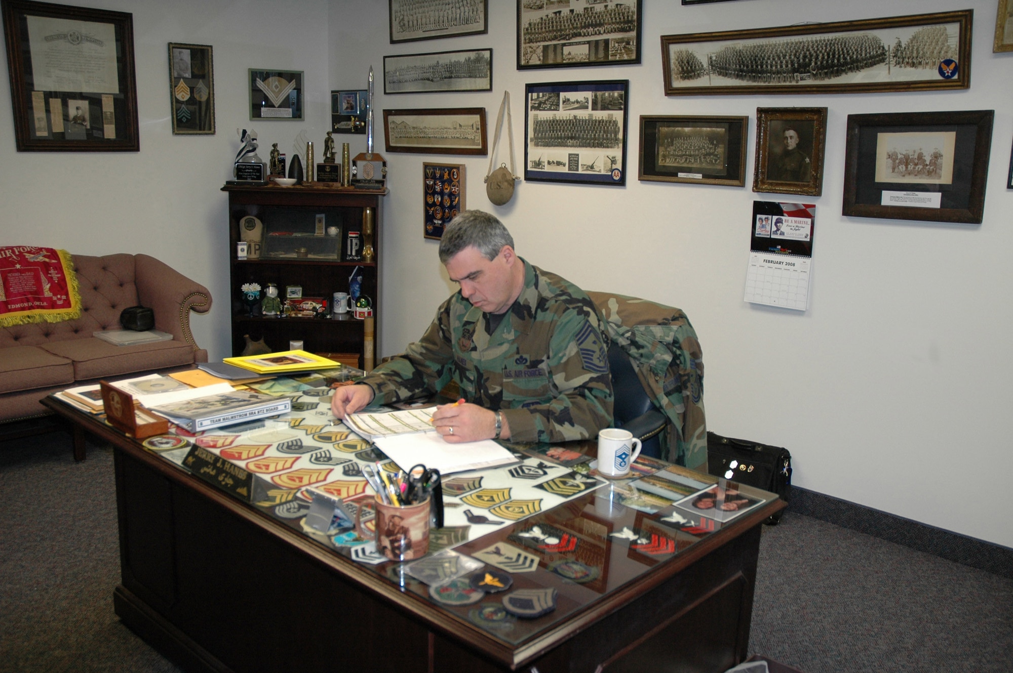 Chief Master Sgt. Jerry Hanes, 341st Operations Group interim-superintendent, jots down notes while working at his desk which displays under glass more than 70 military patches and rank insignia from Civil War to present. Chief Hanes has an extensive military memorabilia collection ranging from uniforms, patches, collar brass, framed photos and documents to name a few. He has been collecting for 35 years. (U.S. Air Force photo/Senior Airman Eydie Sakura)