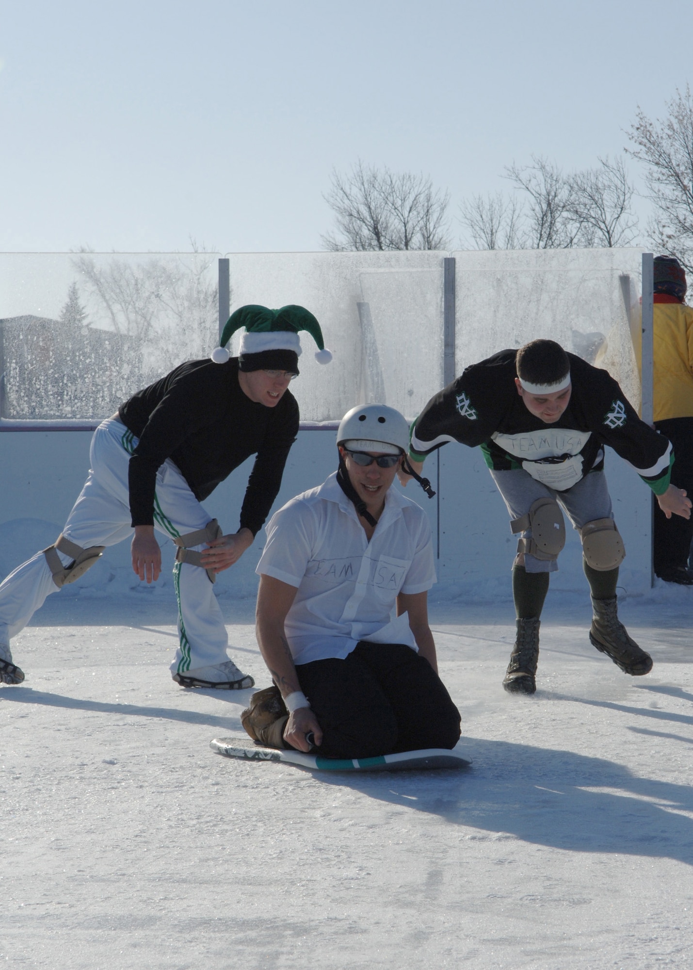 Senior Airman Christopher West, 319th Civil Engineer Squadron, middle, begins to slide after a push from Senior Airman Benjamin Bagnato, left, and Airman 1st Class Geoff Wadsworth, both 319th CES, right, during the Winter Bash?s human curling event at the base ice skating rink. The teams were composed of three members from each Squadron and the winner was judged on far the person on the sled was pushed. (U.S. Air Force phot/Senior Airman Tiffany Colburn)
