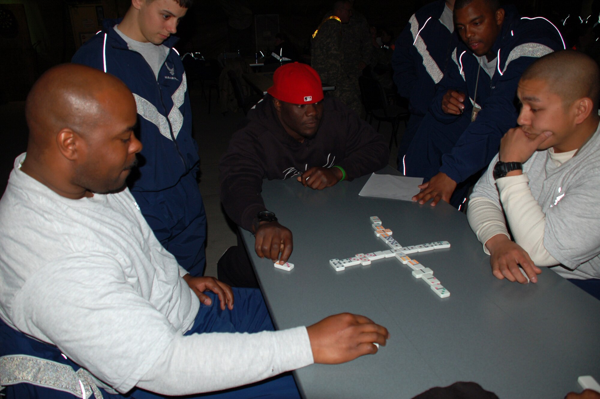 Tommie Harris of the Chicago Bears contemplates his next play during a friendly game of Dominoes with Staff Sgt. Brian Williams (left) and Staff Sgt. Anthony Mayuga March 4 at the recreation center on Manas Air Base, Kyrgyzstan.  Harris, San Diego Chargers Luis Castillo, Carolina Panthers Mike Rucker and Sports Illustrated writer Peter King took park in the United States Organizations National Football League tour to visit servicemembers supporting the war.  They participated in a question and answer session with the Airmen and Soldiers and Marines transiting the base, hanging around afterward to play games and sing Karaoke. (U.S. Air Force photo/Lt. Col. Adriane Craig)