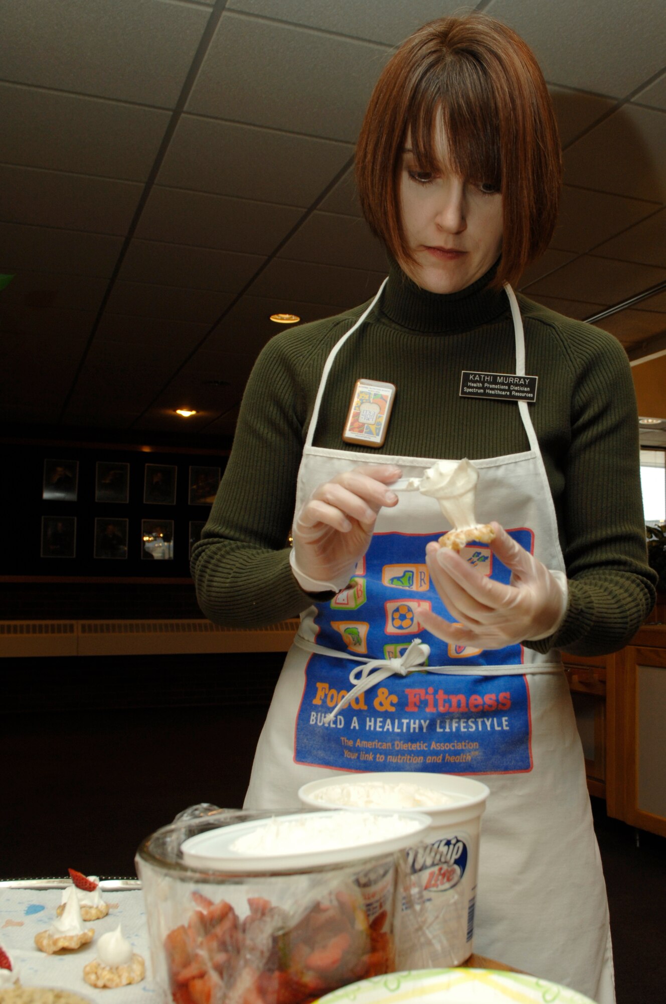 Kathi Murray, 28th Medical Operations Squadron dietitian, dabs lite whipped cream on a rice cake and tops her creation with a sliced strawberry.  The snack, one of many healthy options, was served during a demonstration March 7 at the Bandit Inn for National Nutrition Month. (U.S. Air Force by Airman 1st Class Kasey Zickmund)