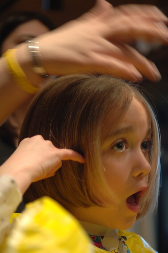 Madeleine Pryor, daughter of Lt. Col. James Pryor, 34th Bomb Squadron commander, expresses her astonishment while having her hair cut to donate to the Locks of Love Organization, March 5.  Fourteen 28th Operations Group spouses, three family members and one enlisted Airman volunteered to donate six to 10 inches of hair to Locks of Love, a non-profit organization that provides hair pieces to financially disadvantaged children under the age of 18; a total of 180 inches of hair was donated. (U.S. Air Force Photo/Airman Corey Hook)