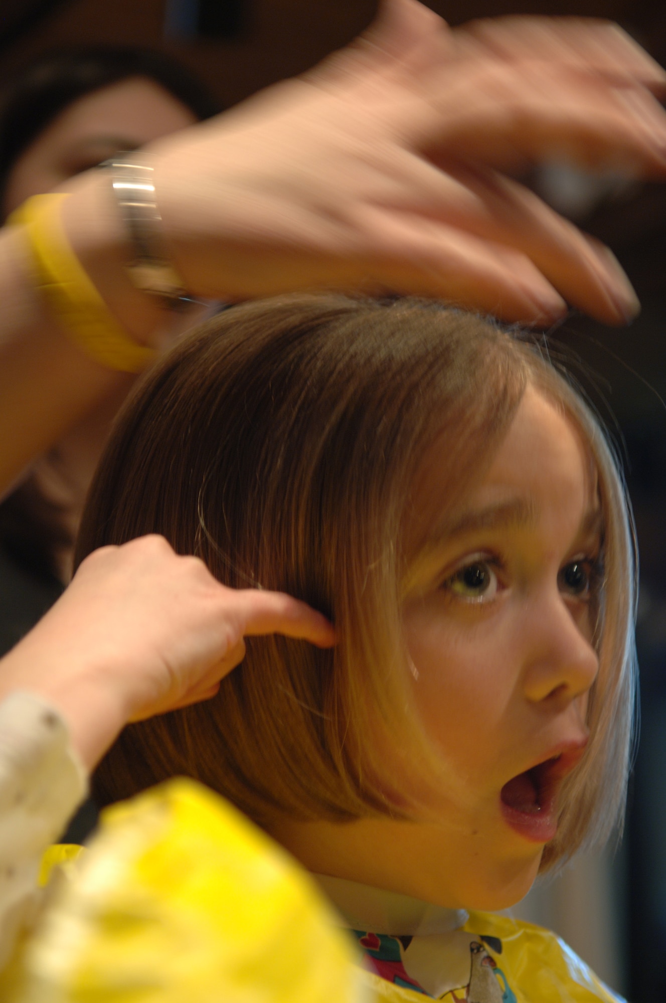 Madeleine Pryor, daughter of Lt. Col. James Pryor, 34th Bomb Squadron commander, expresses her astonishment while having her hair cut to donate to the Locks of Love Organization, March 5.  Fourteen 28th Operations Group spouses, three family members and one enlisted Airman volunteered to donate six to 10 inches of hair to Locks of Love, a non-profit organization that provides hair pieces to financially disadvantaged children under the age of 18; a total of 180 inches of hair was donated. (U.S. Air Force Photo/Airman Corey Hook)