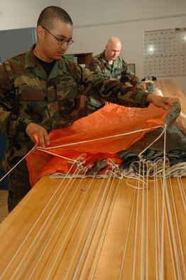 Staff Sgt. Jerry Manley and Senior Airman Patrick Connor, 355th Operations Suport Squadron, parachute shop, inspect the panels of the ACE's II parachute canopy for obvious defects such as holes, tears, and stains.