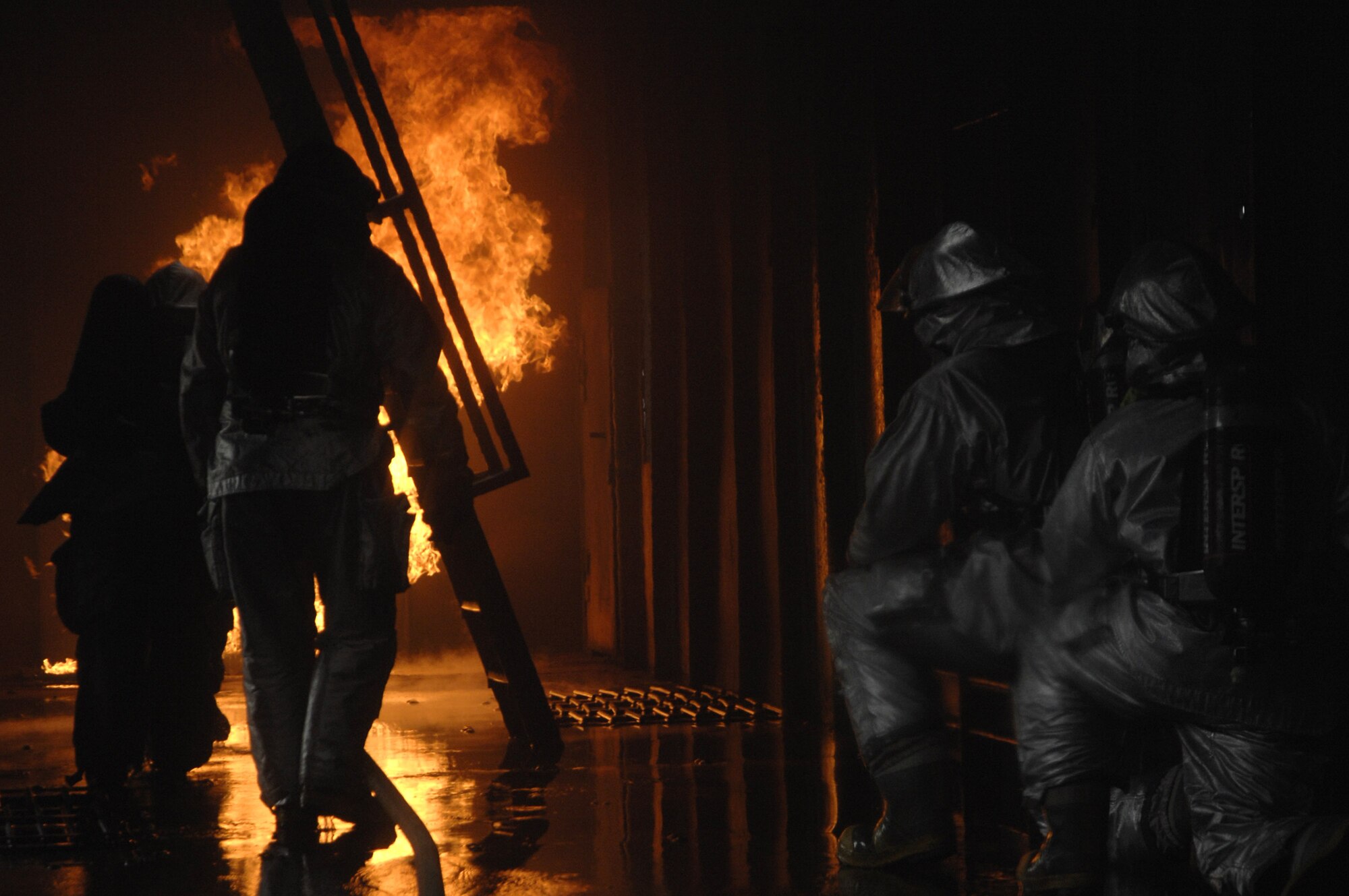 48th Civil Engineer Squadron firefighters advance a hose line toward a simulated cargo fire while another crew backs them up for safety inside an aircraft fire trainer March 8 at Royal Air Force Mildenhall, England. Firefighters must train constantly to stay proficient in their aircraft rescue and firefighting skills. (U.S. Air Force photo/Airman Perry Aston) 
