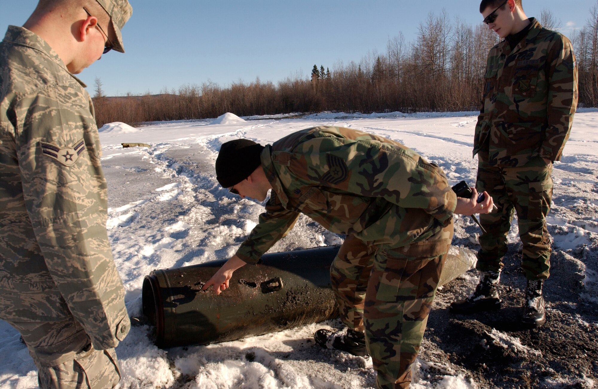 Tech. Sgt. John Moore (center) explains blast damage details to Airmen 1st Class Matthew Leatherman and Dallas Roll after a practice unexploded Ordnance (UXO) was detonated by five pounds of C4 plastic explosive Feb. 21, 2008 at Eielson Air Force Base, Alaska. The detonation provided training to demonstrate the proper and safe procedures for detonating UXO's. (U.S Air Force photo by Staff Sgt. Eric T. Sheler)