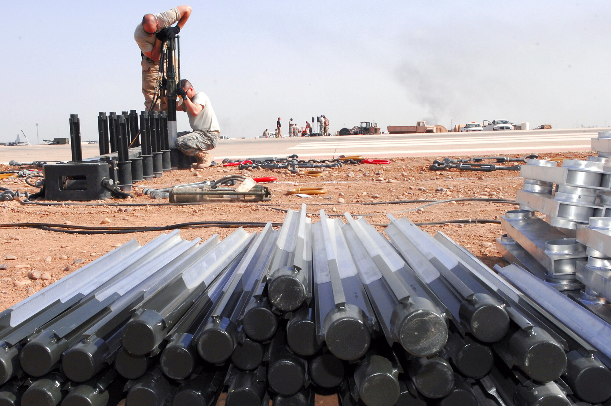 Tech. Sgt. Randy Thibeau and Master Sgt. Gerald Kiger hold a stake hammer as it pounds a four-foot stake into the ground March 12 at Balad Air Base, Iraq. The team drove 168 steaks into the ground to hold the entire arresting barrier system in place. If a fighter aircraft experiences malfunctioning landing gear, the pilot can a drop a hook to catch a cable attached to the barrier system, which slows the aircraft and enables a smoother landing. Sergeant Thibeau is deployed from Ellsworth Air Force Base, S.D.; Sergeant Kiger is deployed from Yokota Air Base, Japan. Both are 332nd Expeditionary Civil Engineer Squadron power production technicians. (U.S. Air Force photo/Senior Airman Julianne Showalter) 