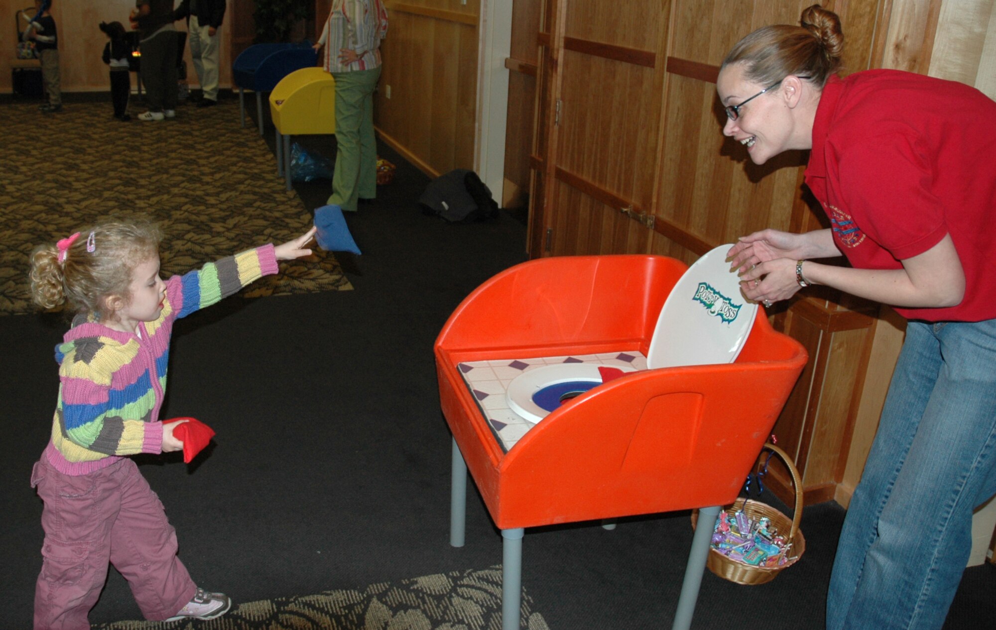 Hannah Smith, 3, tries the Potty Toss game as Tech. Sgt. Jennifer Lyon, Airman & Family Readiness Center, cheers her on. The Potty Toss was just one of many games at the Welcome Home Carnival at Club Hill on March 12.