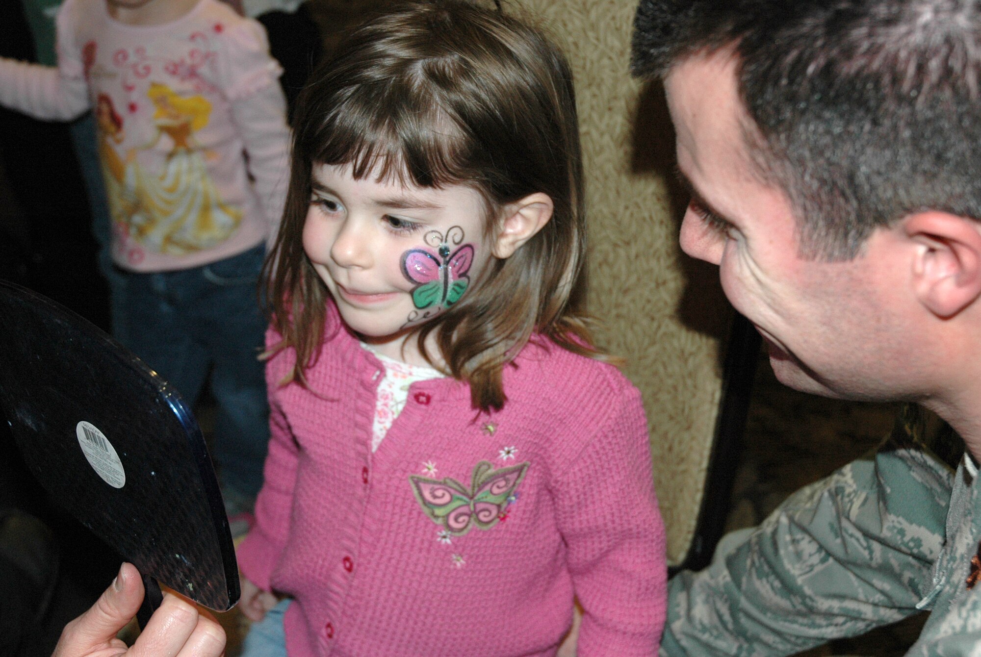 Hannah Becker, 3, smiles as she checks out her new butterfly face painting in a mirror. Maj. James Becker, 518th Combat Sustainment Squadron and Hannah’s dad, brought his daughter to the Welcome Home Carnival at Club Hill on March 12.