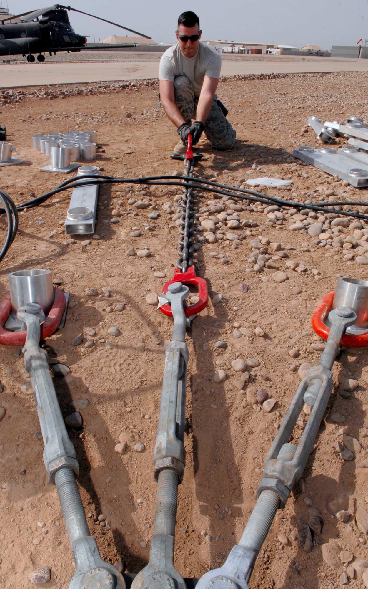 BALAD AIR BASE, Iraq -- Tech. Sgt. Emmanuel Ramirez, 332nd Expeditionary Civil Engineer Squadron power production technician, lays out the turn buckles and spacers before driving four-foot stakes into the ground to prevent the arresting barrier system from shifting during an emergency landing here, March 12. The system is composed of a cable stretched out across the runway attached to a braking system that brings fighter aircraft to a smooth halt during emergency landings. Sergeant Ramirez is deployed form Peterson Air Force Base, Colo. (U.S. Air Force photo/ Senior Airman Julianne Showalter)