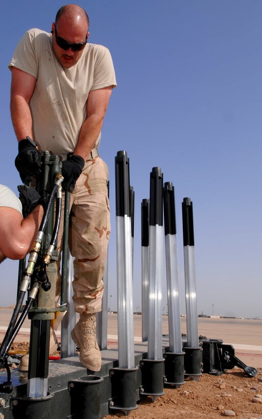 BALAD AIR BASE, Iraq -- Tech. Sgt. Randy Thibeau, 332nd Expeditionary Civil Engineer Squadron power production technician, holds a stake hammer as it pounds a four-foot stake into the ground here, March 12. The stake prevents the arresting barrier system from shifting during an emergency landing. If a fighter aircraft experiences malfunctioning landing gear, the pilot can a drop a hook to catch a cable attached to the barrier system, which slows the aircraft and enables a smoother landing. Sergeant Thibeau is deployed from Ellsworth Air Force Base, S.D. (U.S. Air Force photo/ Senior Airman Julianne Showalter)