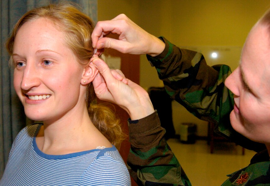 Maj. (Dr.) Teri Simpson applies a small golden stud to the ear of Senior Airman Jillian Sandbothe whose severe headaches resulting from an auto accident where relieved through acupuncture at Landstuhl Regional Medical Center in Germany. (U.S. Army photo/Chuck Roberts) 