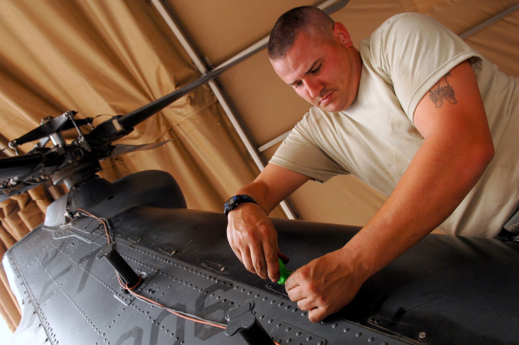 BALAD AIR BASE, Iraq -- Staff Sgt. Tait Delzer, 64th Expeditionary Helicopter Maintenance Unit crew chief, screws in straps that hold in the drive shaft cover of an HH-60G Pave Hawk helicopter here, March 12. A team of Balad crew chiefs performed an inspection on the aircraft after it had been flown 300 hours to ensure all systems and components were performing correctly. Performing preventative maintenance measures is essential to keeping the helicopters functioning and flying. Sergeant Delzer is deployed from Moody Air Force Base, Ga. (U.S. Air Force photo/ Senior Airman Julianne Showalter)