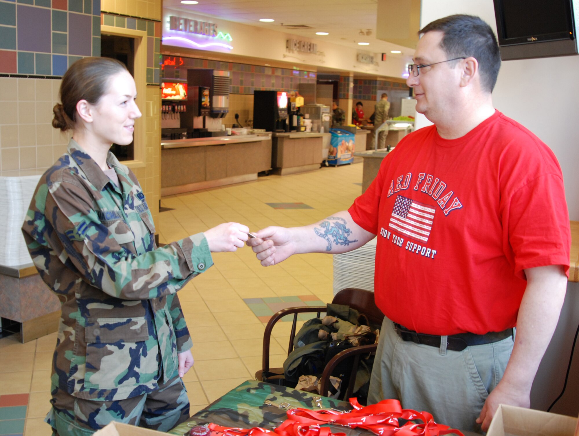 Dennis Mitchell, retired Air Force Staff Sergeant hands a P-38 can opener to Airman 1st Class Christina MacMillian, 22nd Services Squadron, at the Chisholm Trail Dining Facility March 14.  Alongside Bruce Jolly, former Navy Seaman, the two disabled veterans handed out this handy tool, commonly affixed to identification tags, as well as other free outdoor gear to show thanks to Team McConnell members for their service. (photo by Airman 1st Class Jessica Lockoski) 