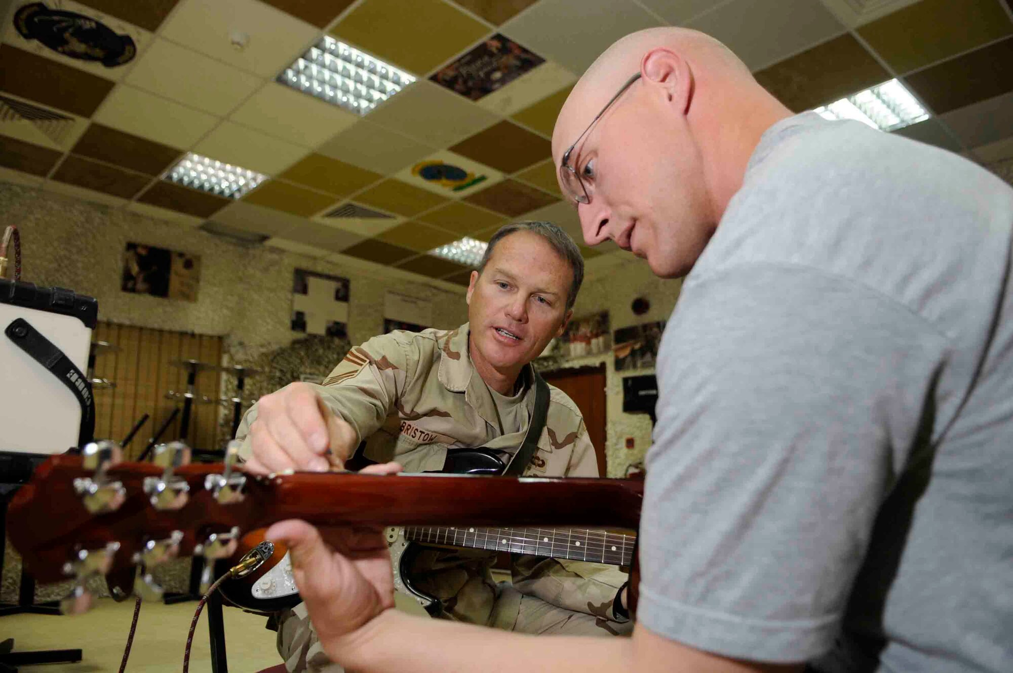 Senior Master Sgt. James Bristow helps 1st Lt. Steven Kline, Alpha 2-43 Air Missile Defense unit, build his guitar chord vocabulary at a Southwest Asia air base March 16. Sergeant Bristow a guitarist and vocalist for the Air Forces Central Band Live Round, performs for service men and women and local communities throughout Southwest Asia.   He is from Manhattan, Kan. deployed from the United States Air Force Academy, Colo. (U.S. Air Force photo/Tech. Sgt. Johnny L. Saldivar)