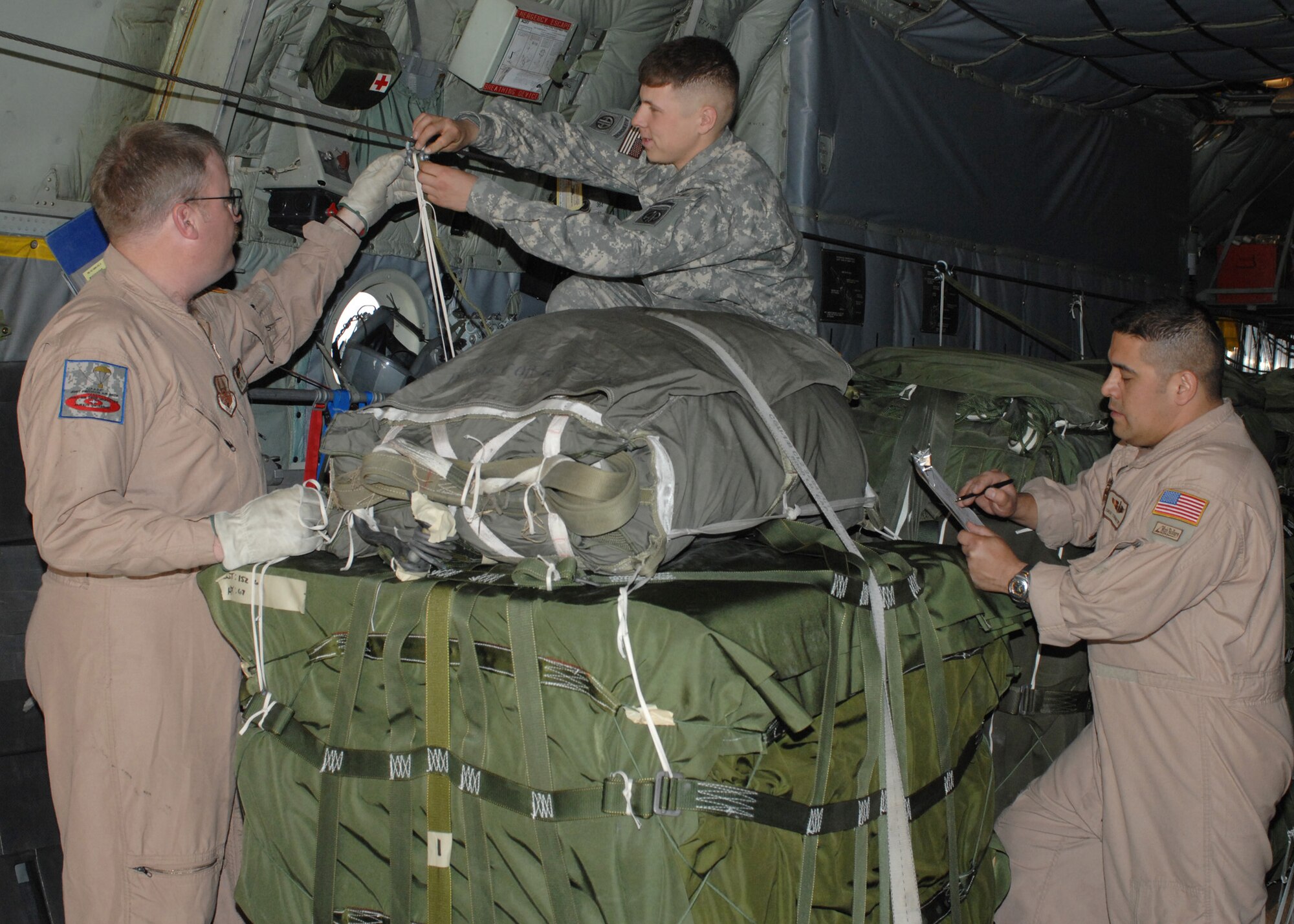 Army Spc. Joshua Black (center) connects a static line to an anchor cable on a C-130 Hercules while joint airdrop inspectors Master Sgt. Mike Pierson (left) from the Delaware Air National Guard's 142nd Airlift Squadron and Senior Master Sgt. Stan Martinez from the 192nd Aerial Squadron at Reno, Nev., inspect the load Feb. 29 at Bagram Air Base, Afghanistan. Specialist Black is an 82nd Airborne rigger with the 11th Quartermaster Detachment. (U.S. Air Force photo/Master Sgt. Demetrius Lester) 